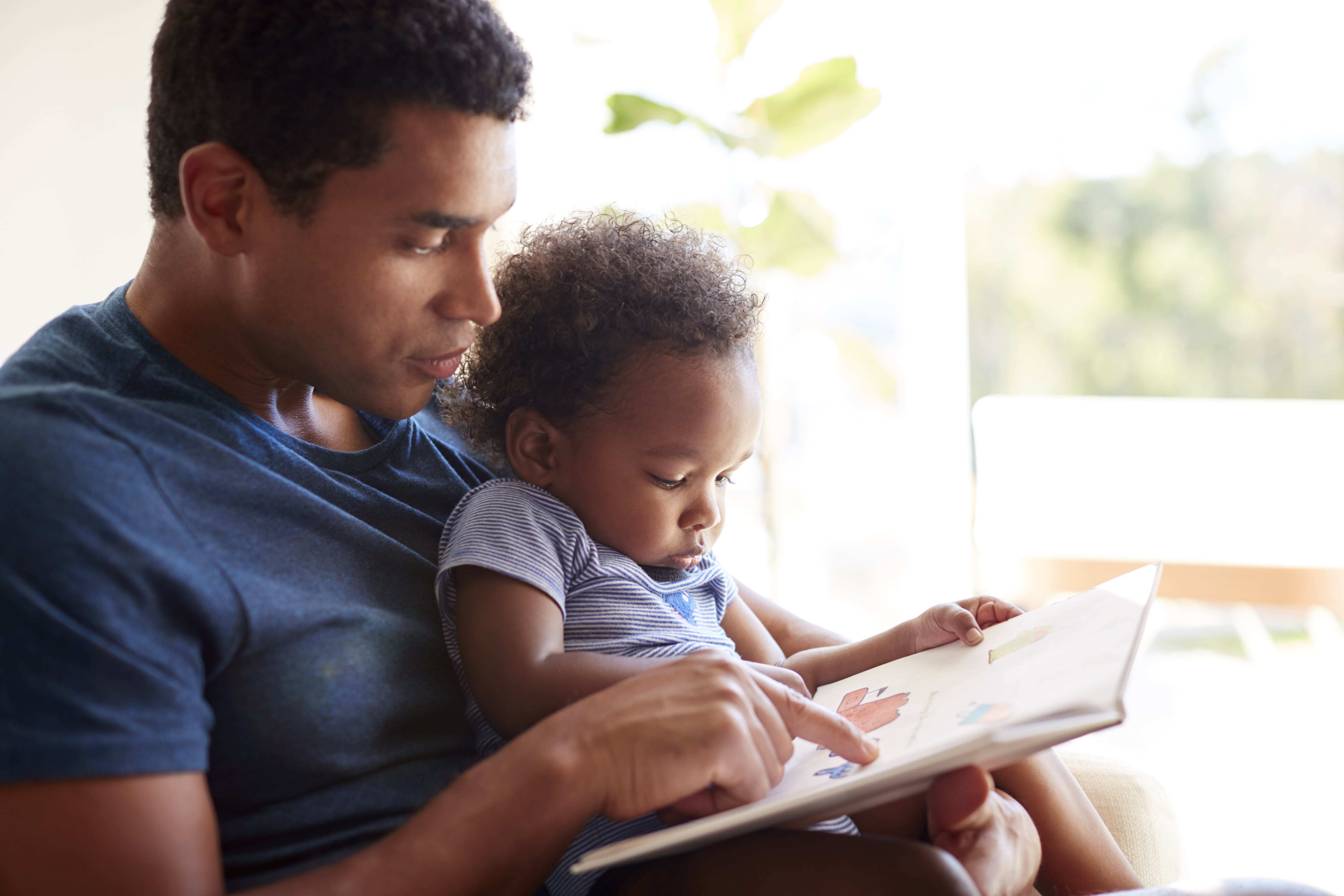 A father reading a book with his Infant child helping to develop language and literacy skills at a young age. 