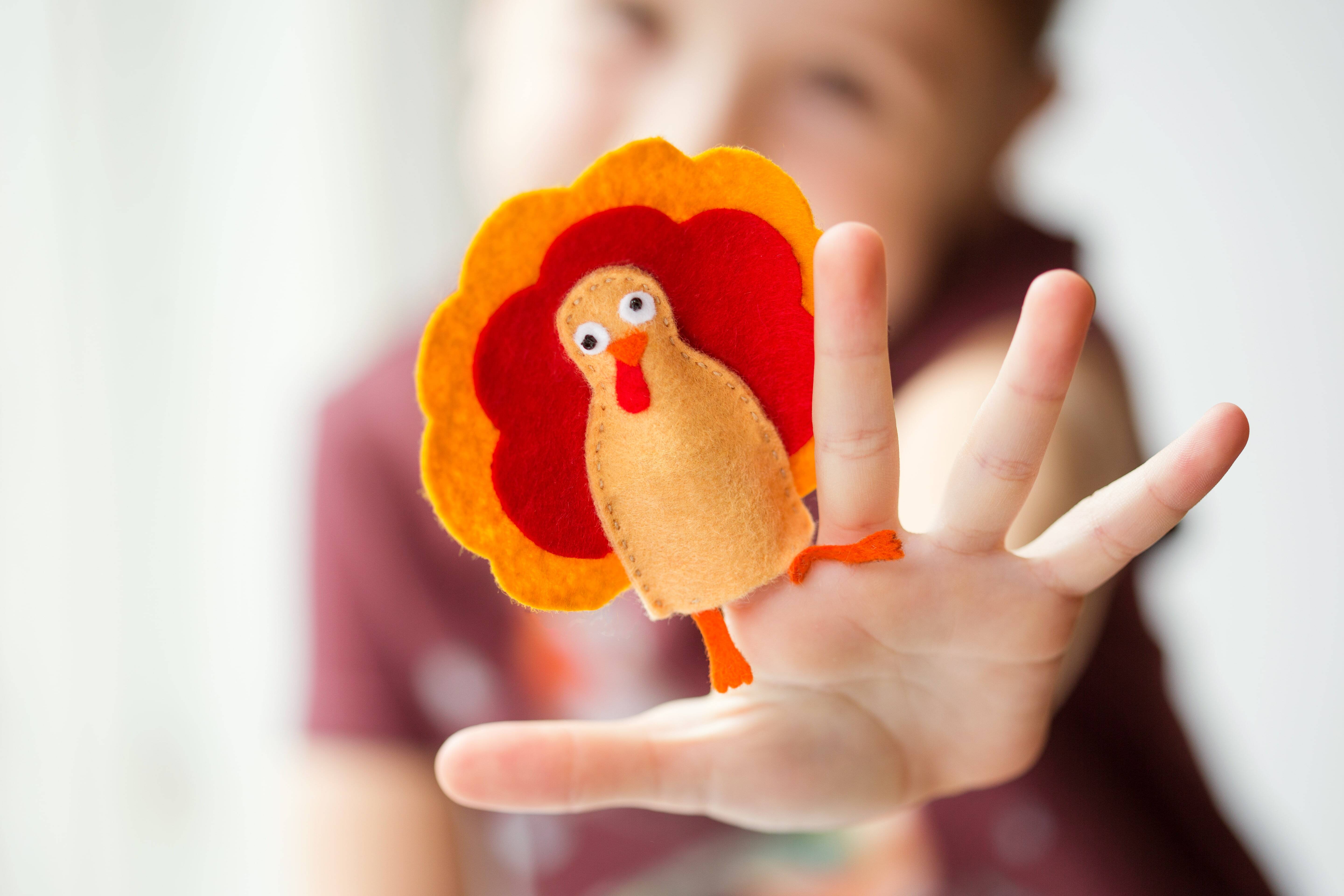 A child showing off their DIY Thanksgiving décor for kids. A child with a DIY turkey finger puppet on their finger. 