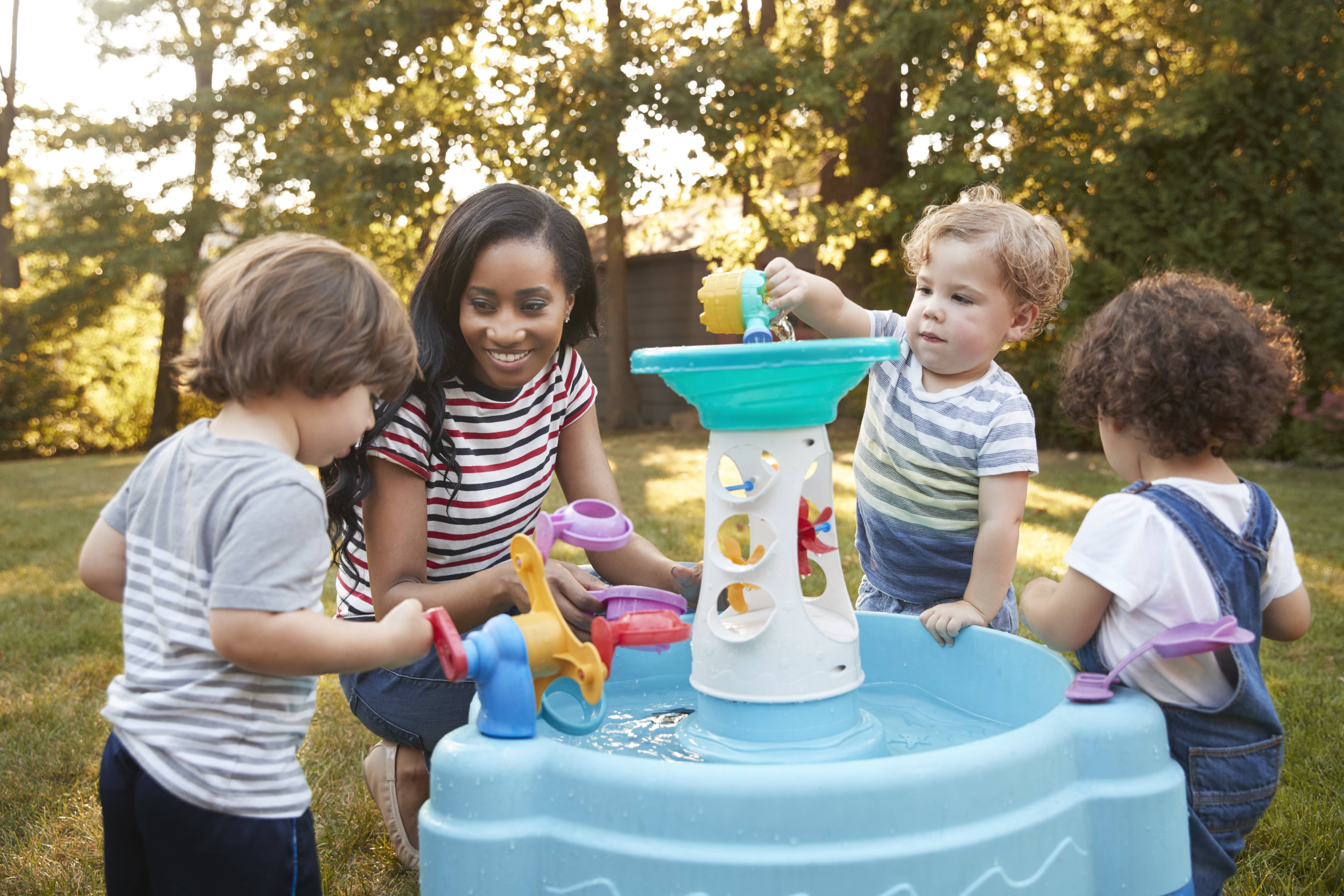 A group of young children playing with water toys outside while an educator guides their learning.  
